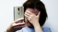 kobieta zakrywająca twarz i trzymająca w dłoni telefon