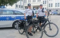 policjant i policjantka przy rowerach, w tle radiowóz