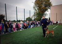 policjant z psem, w oddaleniu spoją dzieci