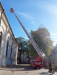 wóz strażacki z wyciągniętym na drabinie koszem, obok stoją policjant i strażacy