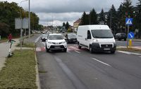 droga, na jezdni stoi osobowa toyota i bus, na porośniętym trawą poboczu stoi hulajnoga elektryczna, w tle inne samochody