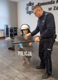 policjant i ubrane w policyjną kamizelkę, kask ochronny i pałkę dziecko