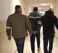 dwaj policjanci w cywilnych ubraniach idą korytarzem z  zatrzymanym mężczyzną