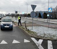 Policjant na jezdni, obok niego za przejściem stoi osobowy Renault, na pasie zieleni stoi hulajnoga elektryczna.