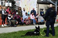 Na trawie leży policyjny pies, obok niego stoi policjant. W rzędzie stoją wychowankowie &quot;Krok za Krokiem&quot;.