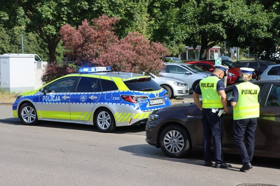 policyjny patrol ruchu drogowego w czasie kontroli pojazdu, obok zaparkowany radiowóz