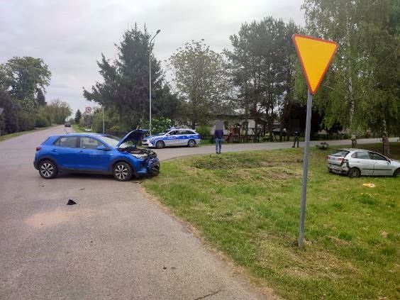 skrzyżowanie dróg, miejsce zderzenia dwóch samochodów, w tle stoi policyjny radiowóz