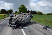 na jezdni na dachu leży osobowe Audi po zderzeniu z Kia, w tle pojazdy i funkcjonariusze służb ratunkowych