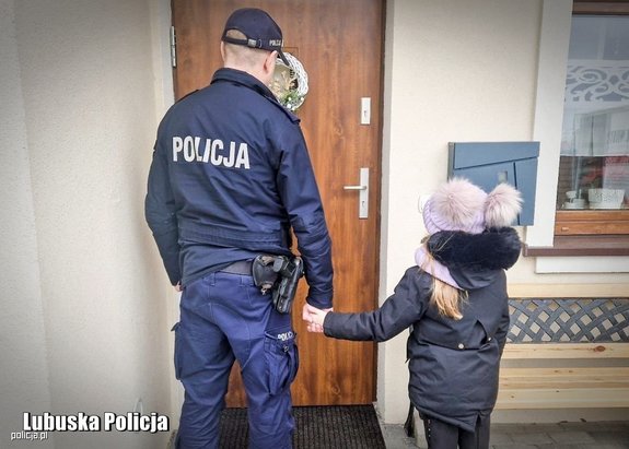przed drzwiami stoi policjant, za rękę trzyma dziecko