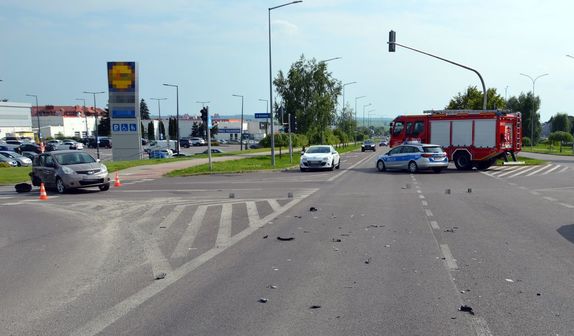 Skrzyżowanie, na którym doszło do zderzenia pojazdów osobowych. Na drodze stoi uszkodzony nissan, radiowóz oraz wóz straży pożarnej.