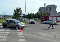 Skrzyżowanie, na którym doszło do zderzenia pojazdów osobowych. Na drodze stoi uszkodzony nissan, radiowóz oraz wóz straży pożarnej. Ulicą idzie policjantka.
