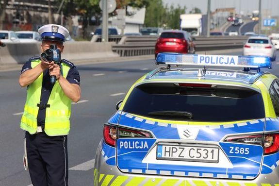 policjant stoi obok radiowozu i mierzy prędkość