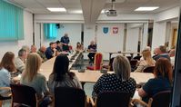 policyjna debata w Zwierzyńcu, za stołami siedzą uczestnicy wraz z policjantami, jeden z policjantów stoi i  mówi do zgromadzonych