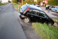 osobowy opel w rowie po uderzeniu w betonowy przepust, w tle parking przed sklepem, po którym idzie mężczyzna oraz policjant, na parkingu kilka zaparkowanych samochodów i policyjny radiowóz