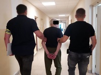 zatrzymany prowadzony przed dwóch policjantów w cywilnym ubraniu