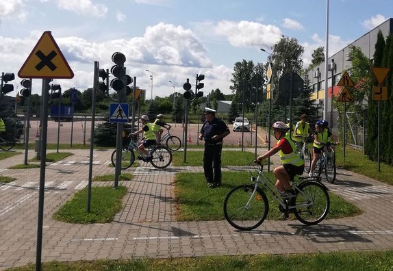 policjant i jeżdżący na rowerach uczniowie na miasteczku rowerowym w czasie egzaminu na kartę rowerową