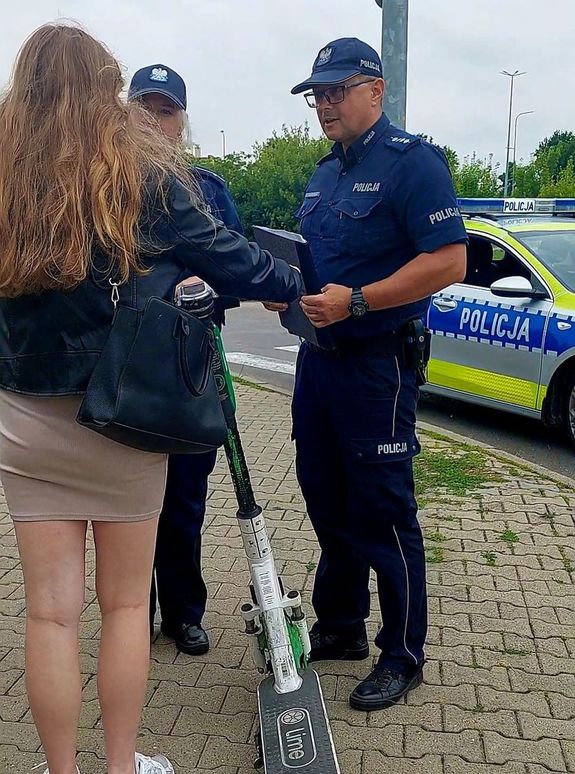 policjanci i kierująca hulajnogą elektryczną w tle radiowóz