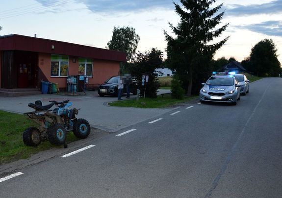 na poboczu drogi stoi quad i dwa radiowozy, w tle budynek
