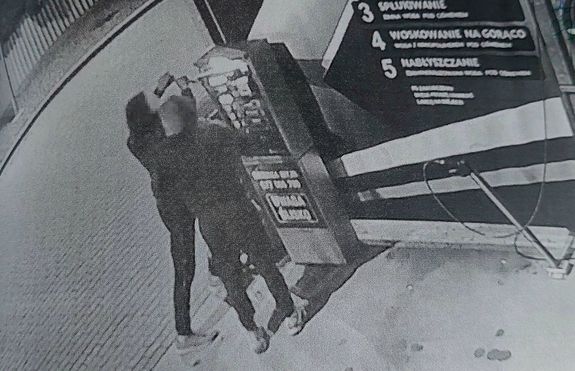 zdjęcie z nagrania z kamery dwaj mężczyźni przy urządzeniu do wpłacania pieniędzy na myjni samochodowej