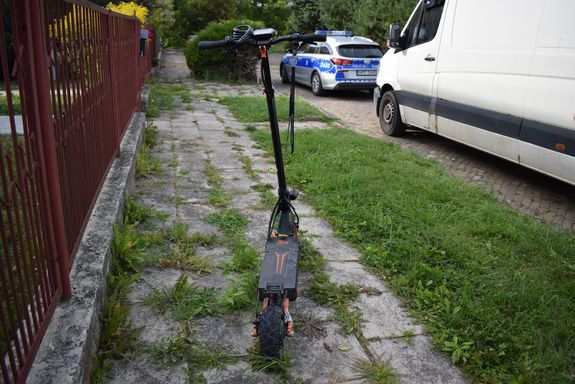 na chodniku stoi hulajnoga elektryczna, na jezdni obok zaparkowany bus i radiowóz