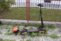 na chodniku stoi hulajnoga elektryczna, obok niej leży kask