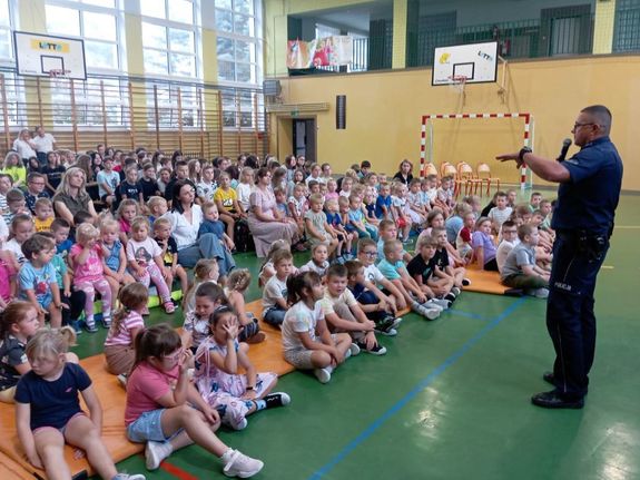 zdjęcie ze spotkania profilaktycznego w szkole, uczniowie siedzą na ławeczkach przed nimi policjant mówi im o zasadach bezpieczeństwa