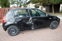 na podjeździe stoi osobowa Dacia z bocznymi wgnieceniami