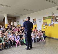 policjant mówi do siedzących na ławeczkach dzieci w czasie spotkania profilaktycznego