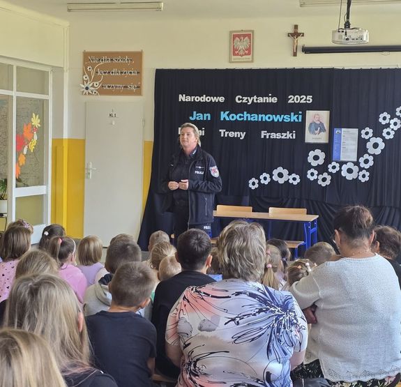 policjantka mówi do siedzących na ławeczkach dzieci w czasie spotkania profilaktycznego