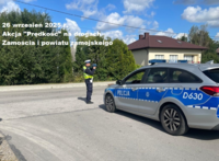 policjant stoi na poboczu drogi i mierzy prędkość, obok niego stoi radiowóz