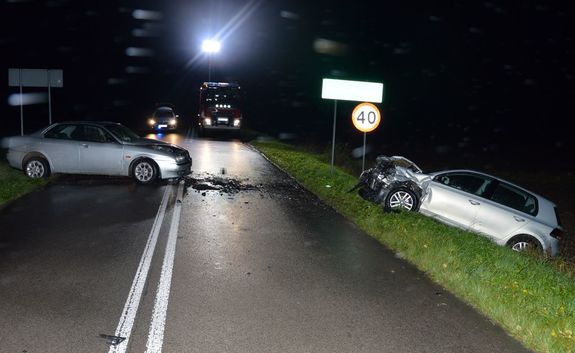 Droga, miejsce wypadku. Na jezdni w poprzek stoi osobowa Alfa Romeo, w przydrożnym rowie osobowy Volkswagen. W tle policyjny radiowóz i wóz strażacki.