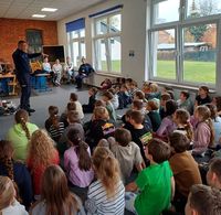 policjant rozmawiający z siedzącymi na dywanie i krzesełkach dziećmi, w czasie spotkania profilaktycznego