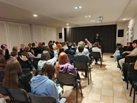 policjant stoi przed uczniami siedzącymi na krześle w czasie spotkania profilaktycznego