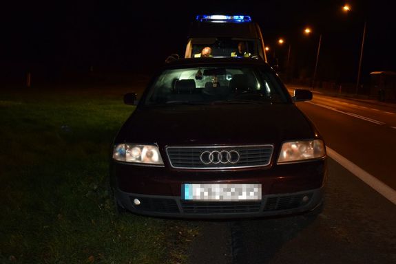 zaparkowane na poboczu drogi osobowe audi i stojący za nim radiowóz, w którym siedzą dwaj policjanci
