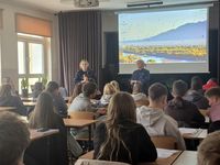 dwie policjantki w czasie spotkania profilaktycznego w szkole rozmawiają z siedzącą na krzesłach młodzieżą