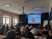 dwie policjantki w czasie spotkania profilaktycznego w szkole rozmawiają z siedzącą na krzesłach młodzieżą