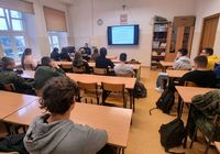 policjant siedzi za biurkiem a młodzież na krzesłach przy ławkach, lekcja w klasie o profilu mundurowym