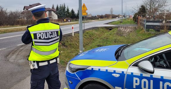 przy radiowozie stoi policjant i mierzy prędkość jazdy