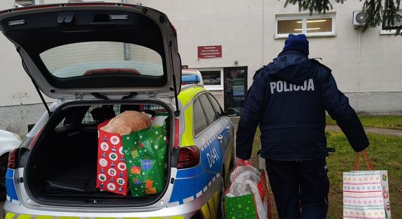 policjantka niesie prezenty dla dzieci, obok stoi radiowóz z otwartym bagażnikiem, w którym są opakowania z prezentami