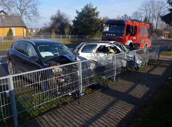 osobowy fiat i ford uszkodzone po zderzeniu stoją na poboczu drogi przed barierką oddzielającą jezdnie od chodnika, za nimi na ulicy stoi wóz strażacki
