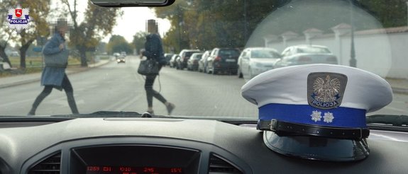 dwie osoby przechodzące przez przejście, zdjęcie zrobione z radiowozu, na kokpicie radiowozu leży czapka policjanta ruchu drogowego