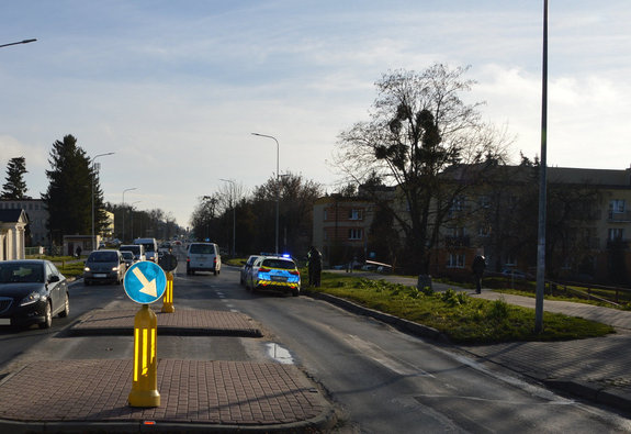 miejsce zdarzenia drogowego - potrącenia pieszej na oznakowanym przejściu dla pieszych, widoczna jest ulica, przejście dla pieszych, oznakowany radiowóz i przejeżdżające samochody
