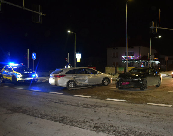 skrzyżowanie dróg, dwa samochody osobowe po zderzeniu, za nimi stoi policyjny radiowóz