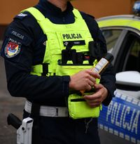 policjant trzymający w ręku alkomat, w tle radiowóz