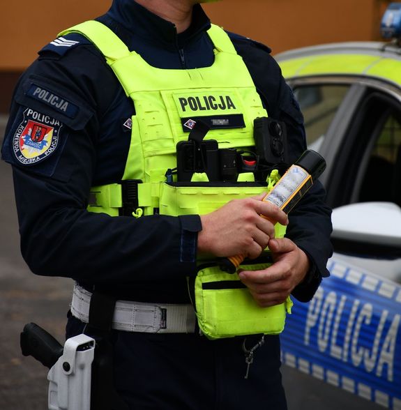 policjant trzymający w ręku alkomat, w tle radiowóz