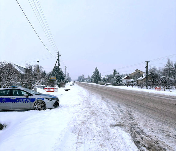 radiowóz stoi na ośnieżonym poboczu, zaśnieżona droga