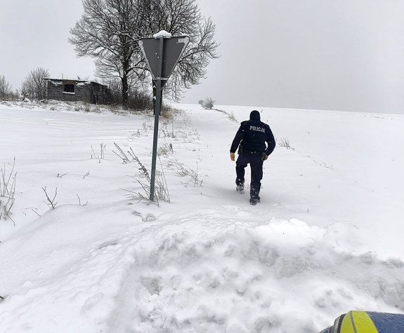 idący zaśnieżoną drogą policjant
