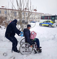 policjant pcha wózek inwalidzki z mężczyzna, w tle policyjny radiowóz