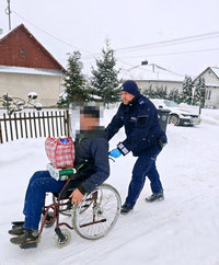 policjant pcha wózek inwalidzki z mężczyzna po zaśnieżonej drodze