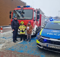 policjant z dziećmi przed wozem bojowym strażaków, obok policyjny radiowóz